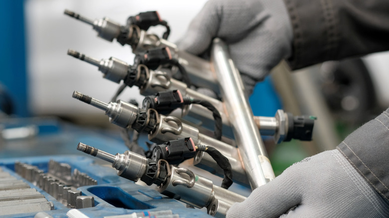 A technician wearing white gloves handling a fuel rail and a set of fuel injectors.