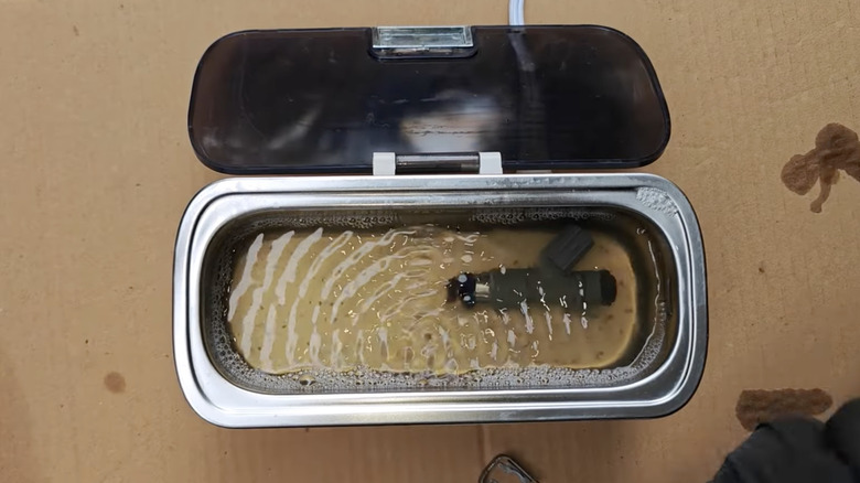 A fuel injector submerged in an ultrasonic cleaner.