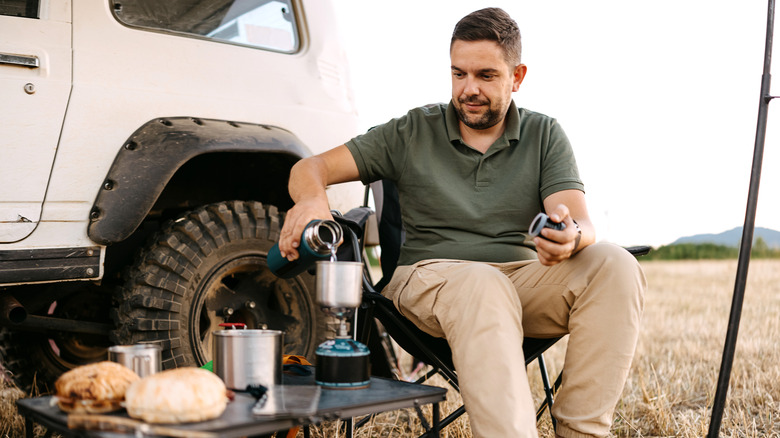 Man making coffee with camping stove sat next to his SUV
