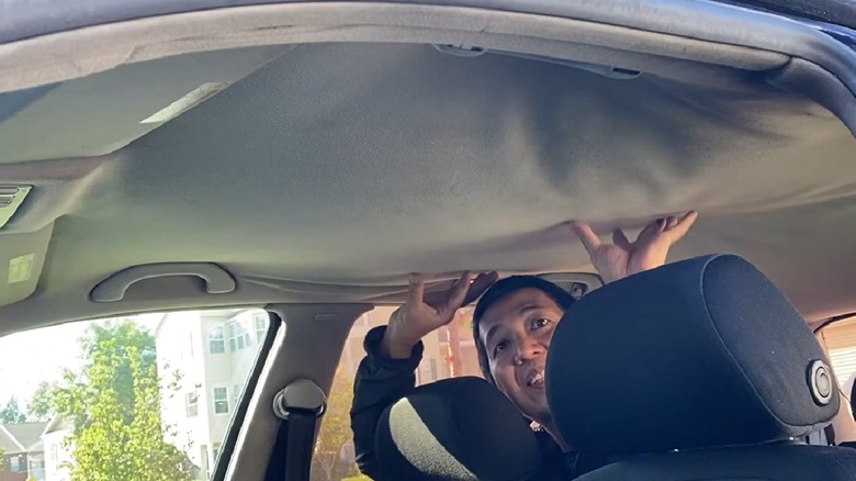 A man holding up a droopy car headliner
