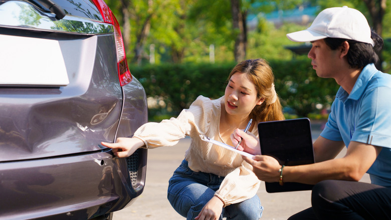 Two people inspecting a big dent on the rear of a car