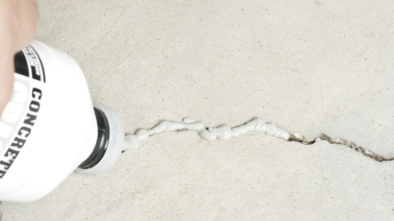 A held bottle filling a concrete crack with cement