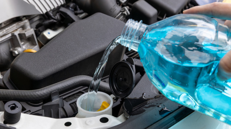 A person owner refilling the windshield washer reservoir with blue washer fluid.