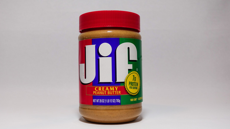 Jar of creamy Jif peanut butter on white-gray background.