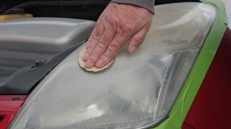A person sanding a headlight by hand as part of a restoration