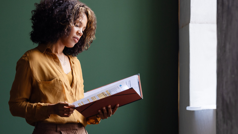 A woman leafs through a folder of papers near a window.