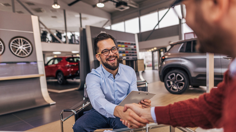 A man smiles and shakes hands in a car dealership.