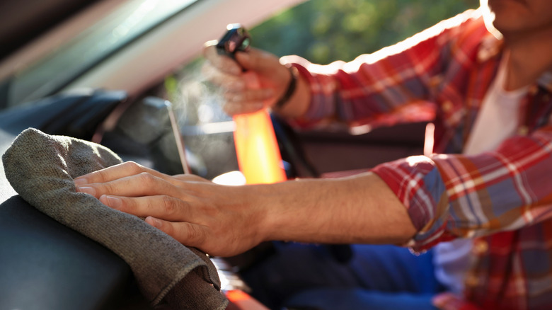 A person cleaning the dashboard with spray solution and cloth
