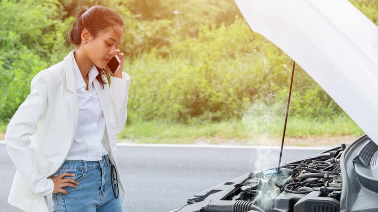 Woman on phone looking at overheated car engine