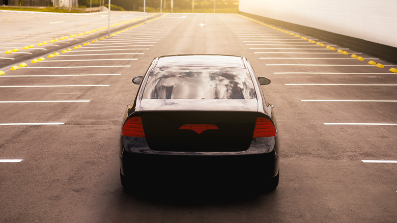 A black car driving on an empty parking lot