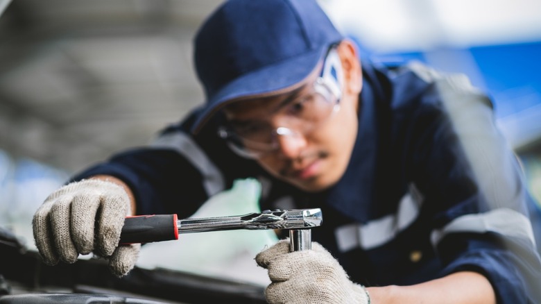 A mechanic wearing fabric gloves turning a ratchet pinch a socket