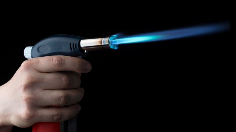 Hand holding a lit butane torch