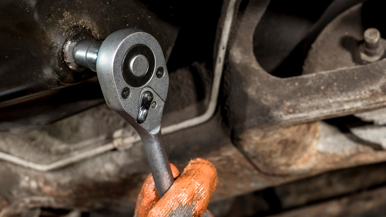 Mechanic using a socket wrench to turn the oil drain plug