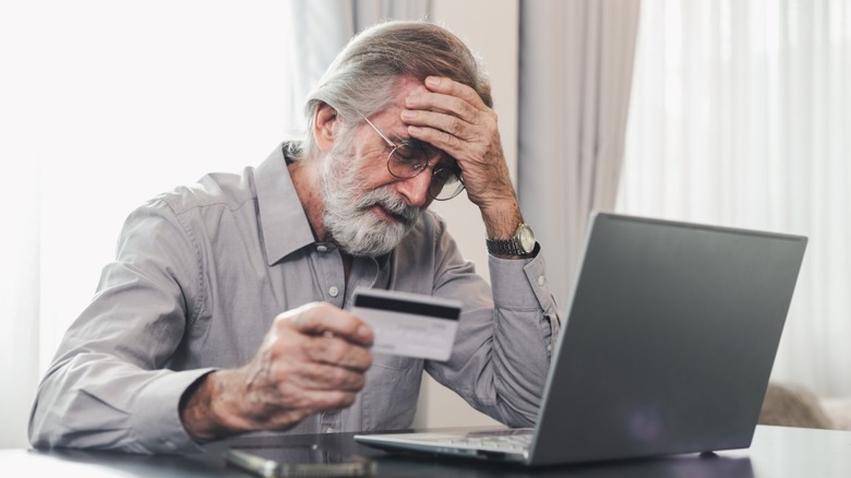 Older man sitting in front of laptop holding a credit card worried about being scammed