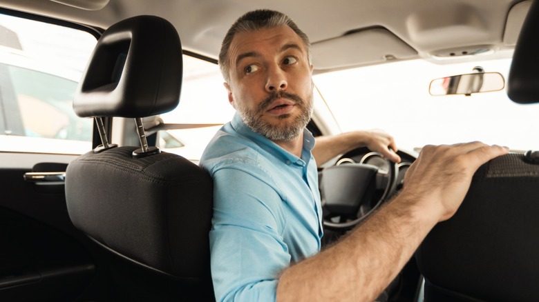 A person driving in reverse in their car while looking over their shoulder