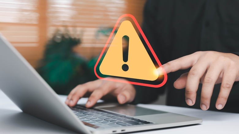 Person using laptop with large holographic warning sign floating above the keyboard