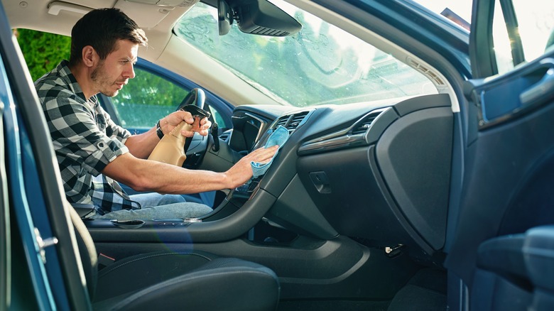 A man cleaning a car dashboard with spray.