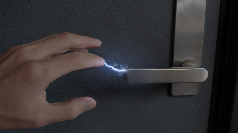A person reaching for a metal door handle with a static electricity visible