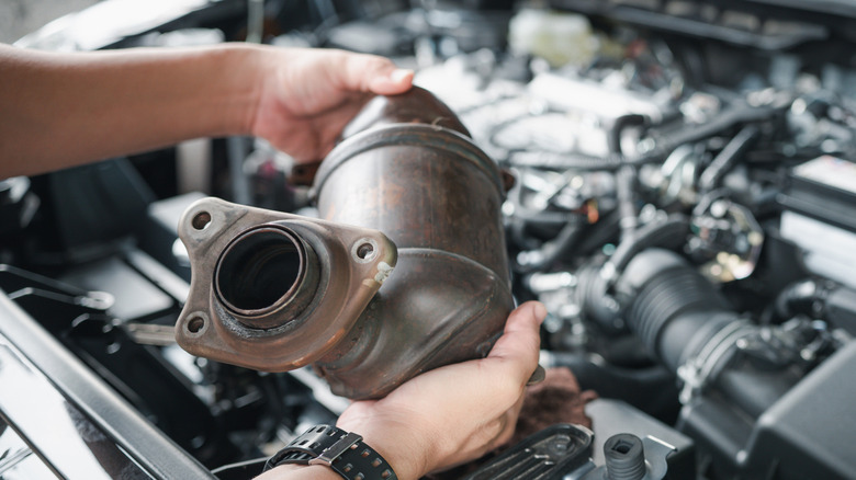 Mechanic holding an old catalytic converter over an engine bay