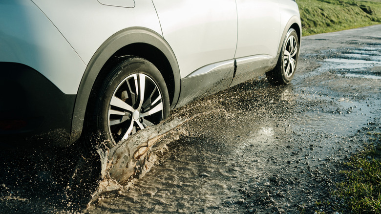 A crossover driving over potholes on wet, rugged terrain