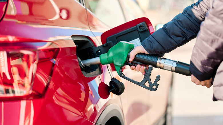 Photo of a person filling up a red car with fuel, holding the pump nozzle.