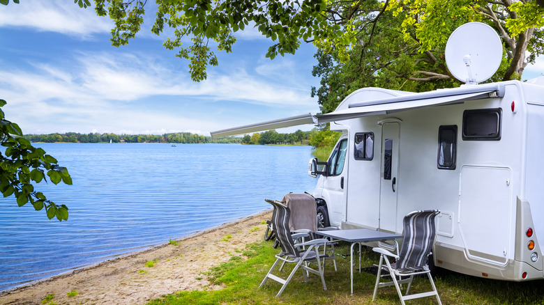 An RV parked on a lake shore using a satellite antenna and solar panels.