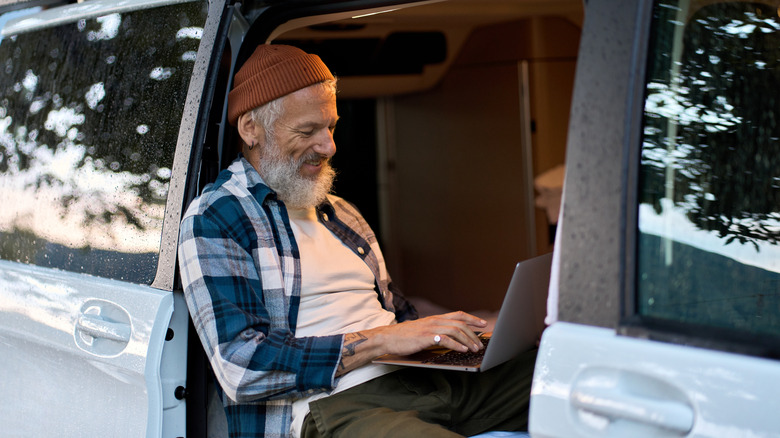 A man taps on a laptop in the open door of an RV.