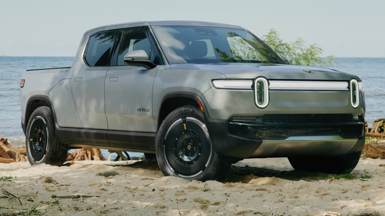 A Rivian R1T parked on a sandy beach with a large body of water in the background