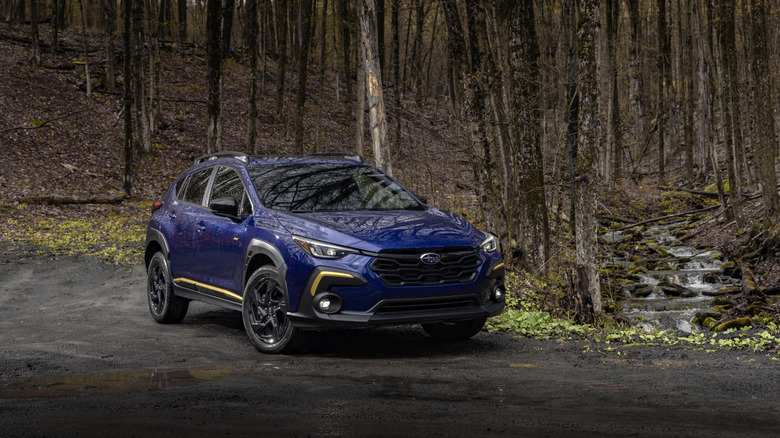 A front right 3/4 of a blue Subaru Crosstrek in front of trees in a forest.