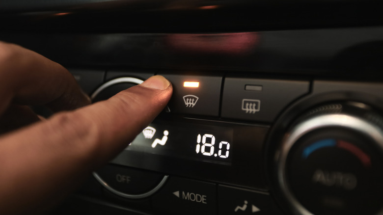 Hand pressing the defogger button to clear a car's windshield