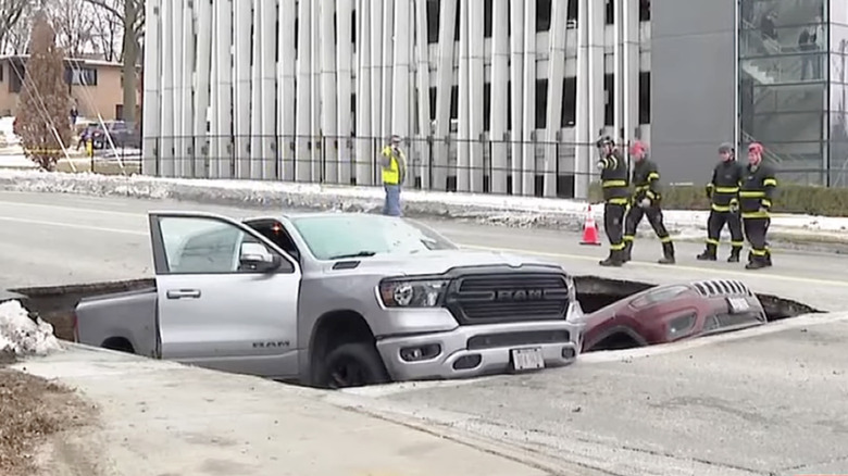 A Ram pickup and a Jeep inside a sinkhole in Omaha, Nebraska, as firefighters look on
