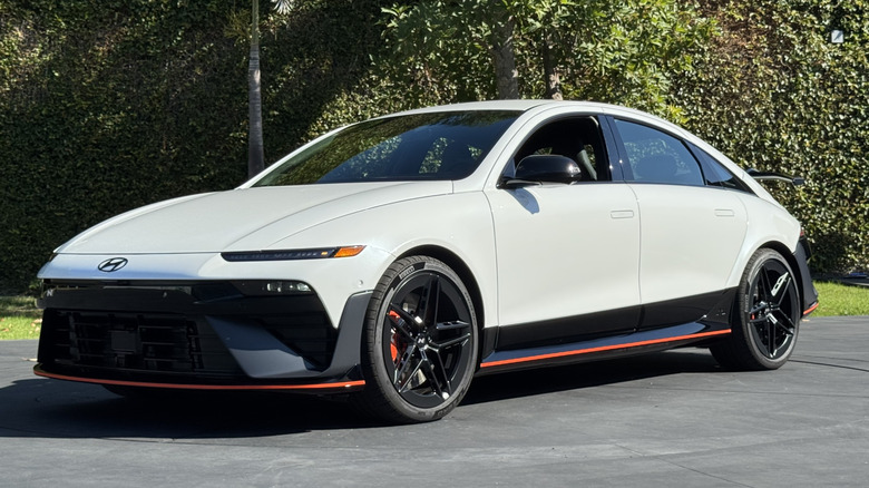 A front three quarters shot of a white Ioniq 6 N parked on blacktop in front of grass and a hedge