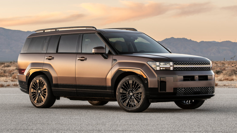 Front front three-quarters shot of a brown 2027 Hyundai Santa Fe parked in front of a desert sunset