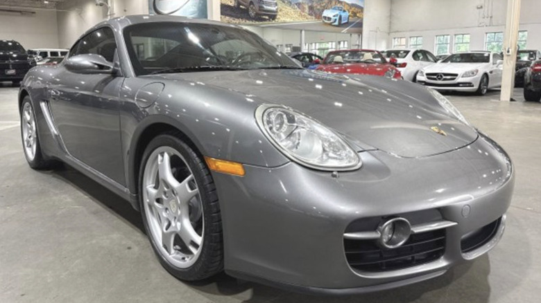 a silver Porsche Cayman parked indoors with other luxury vehicles.