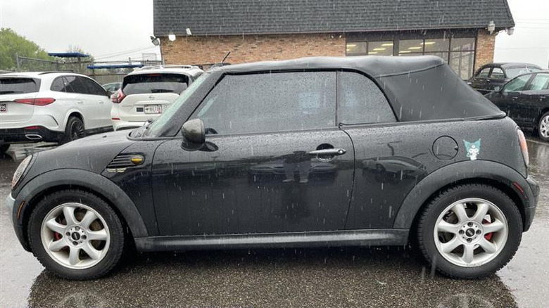 a black mini cooper s photographed in a used car lot on a rainy day