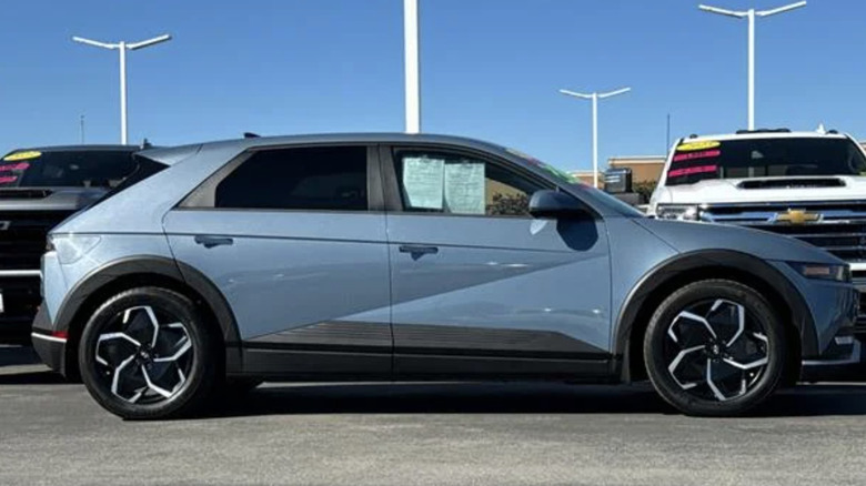 a blue Hyundai Ioniq 5 parked in a car dealership parking lot on a cloudless day