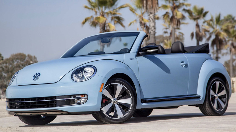 A blue Volkswagen Beetle convertible parked in front of palm