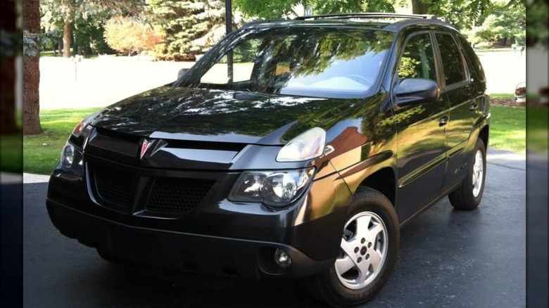 A black, 2002 Pontiac Aztek in a driveway, reflecting its surroundings in the glossy paint.