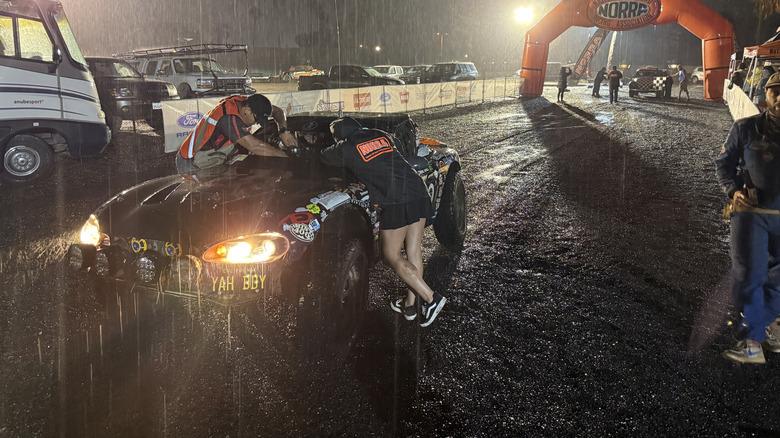 Two people working hard on a an off-road miata in the pouring rain at night