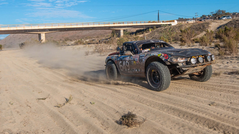 An off-road Miata driving down a dirt road, a plum of dust in its wake