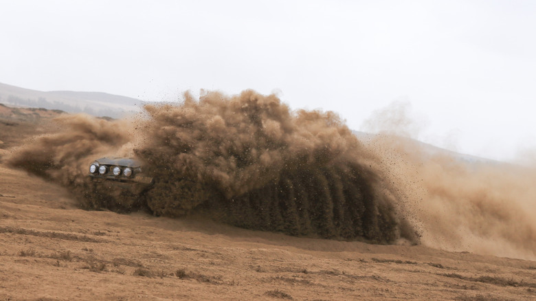 An off-road Miata obscured by a big cloud of dust, just the headlights visible.
