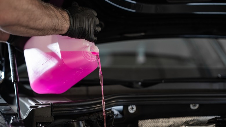 Mechanic topping off a car's coolant with a pink coolant