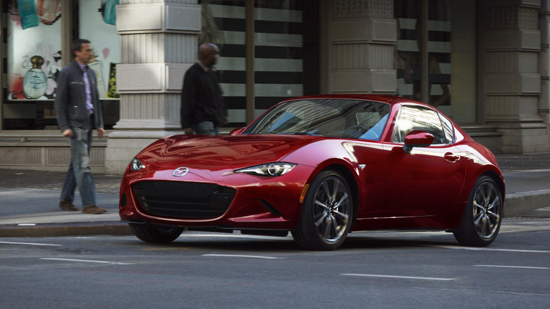 A red Mazda MX-5 RF with no front license plate on a city street