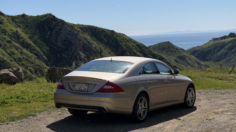 Rear 3/4 view of a gold Mercedes-Benz CLS with the ocean in the background