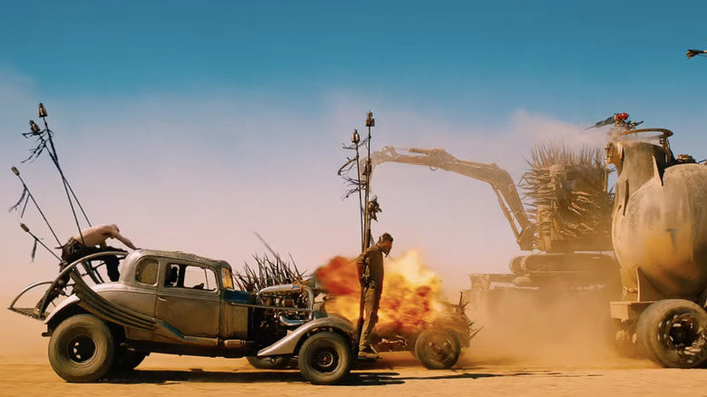 Screenshot from Mad Max: Fury Road showing cars driving with an explosion behind