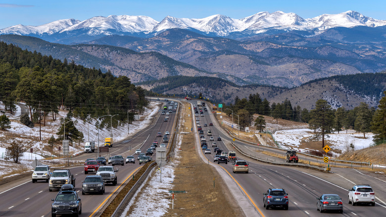 A sunny Winter day view of busy Interstate Highway I-70, with snow-capped high peaks of Continental Divide towering at west.