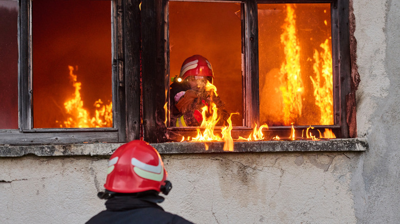 One firefighter inside burning building at window, one outside watching