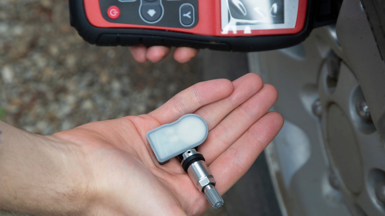 A man holding a TPMS sensor and a sensor programmer