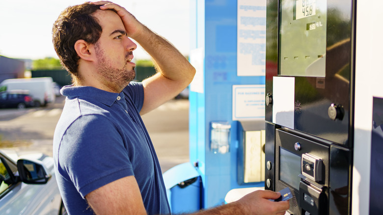 A man holds his head when seeing how expensive fuel is while paying at the pump.