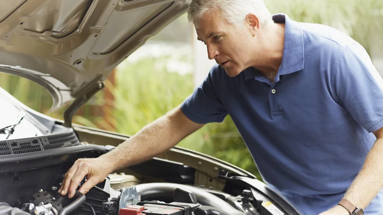 An older man looking at a car engine.